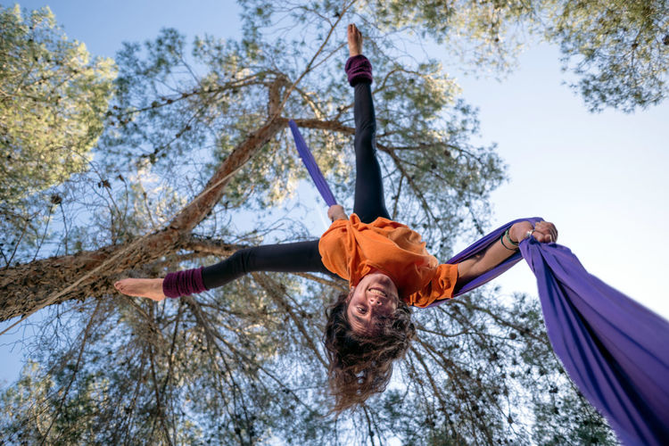 Young girl acrobat. practicing aerial silks. woman doing circus stunts with clothes in the forest. straddle fall position.