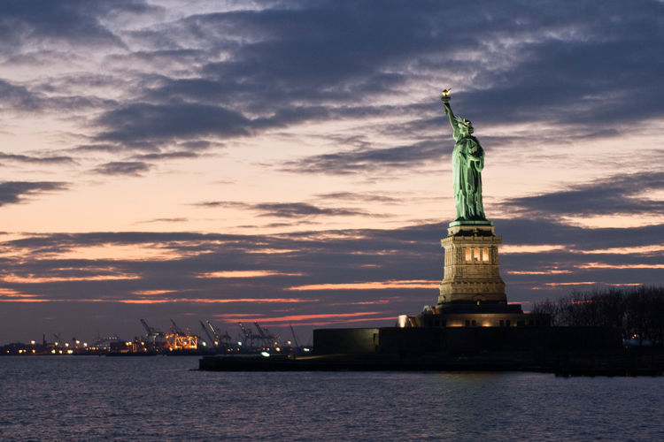 Statue of liberty against cloudy sky at dusk