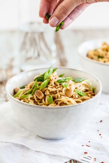 Cropped hand of woman adding chopped scallions to noodles in bowl on table