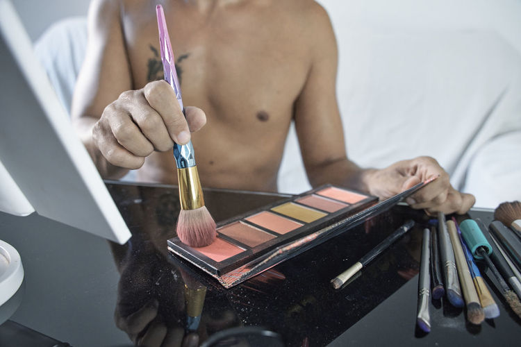 Man taking blush from palette with brush while sitting at table