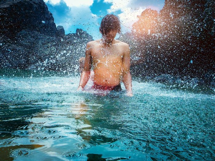 Shirtless man splashing water in sea against mountains