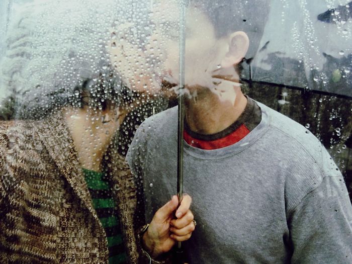 Couple kissing while holding umbrella in rainy season