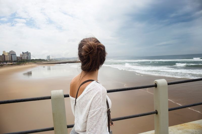 Woman looking at beach while standing on bridge against sky