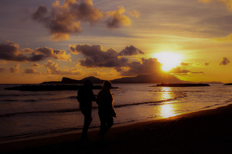 Silhouette women on beach against sky during sunset