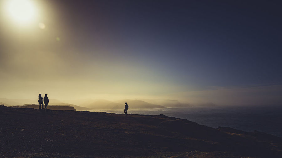 Silhouette people standing on mountain by sea against sky during sunset
