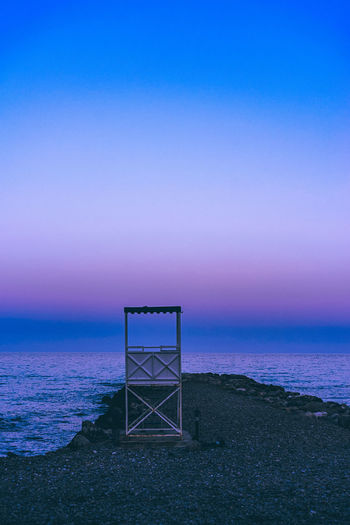 Lifeguard chair at beach against sky during sunset