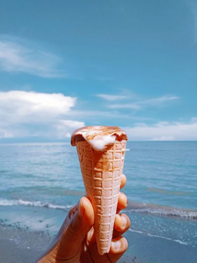 Midsection of person holding ice cream in sea against sky