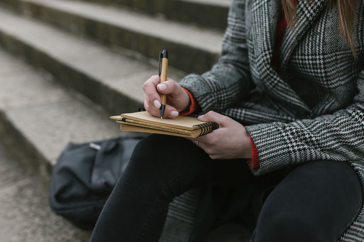 Woman writing in book while sitting on steps