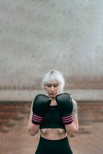 Woman with boxing gloves standing against wall