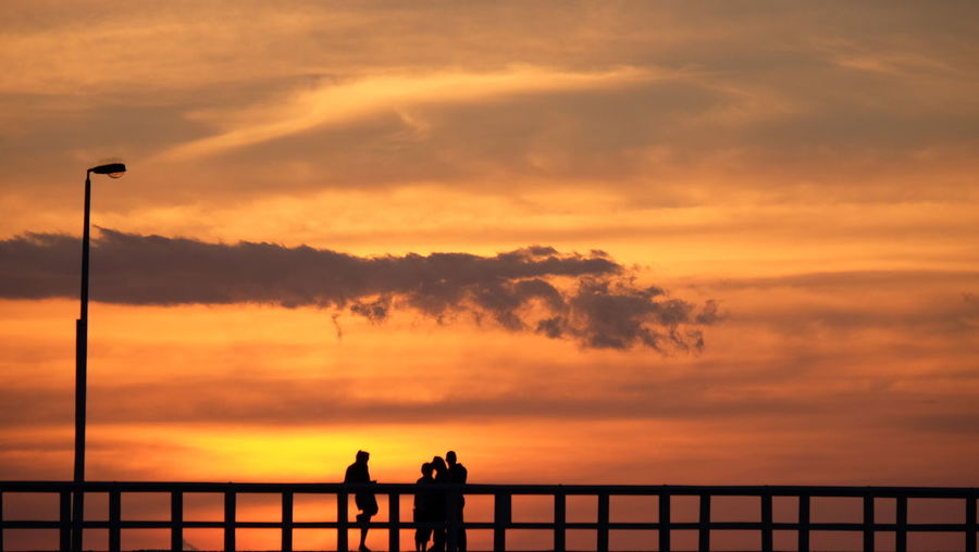 Silhouette people by sea against dramatic sky during sunset