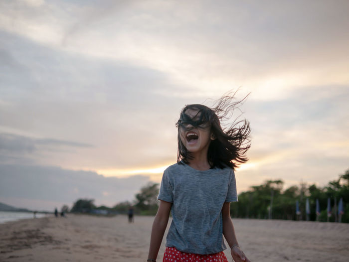 Happy girl screaming at beach against sky during sunset