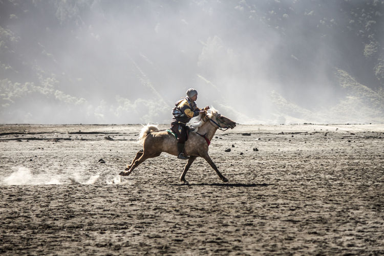 Men riding horse on sand against sky
