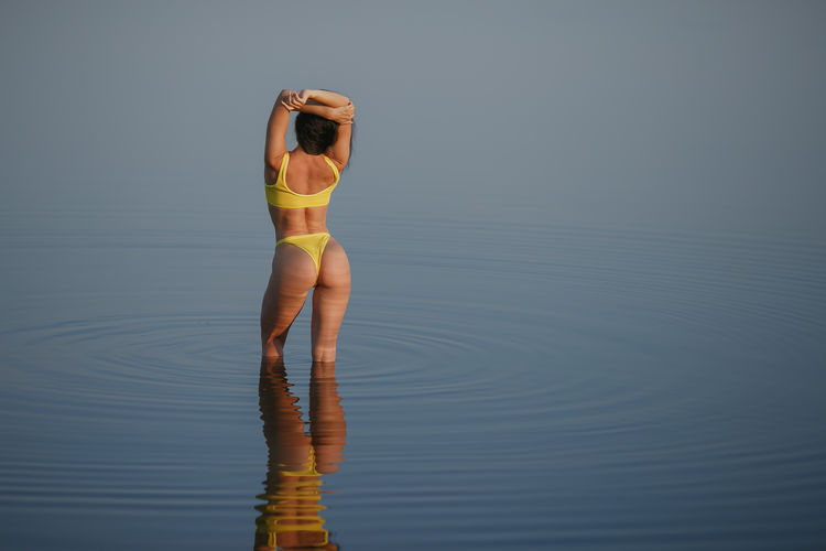 Rear view of seductive woman wearing yellow bikini while standing in sea