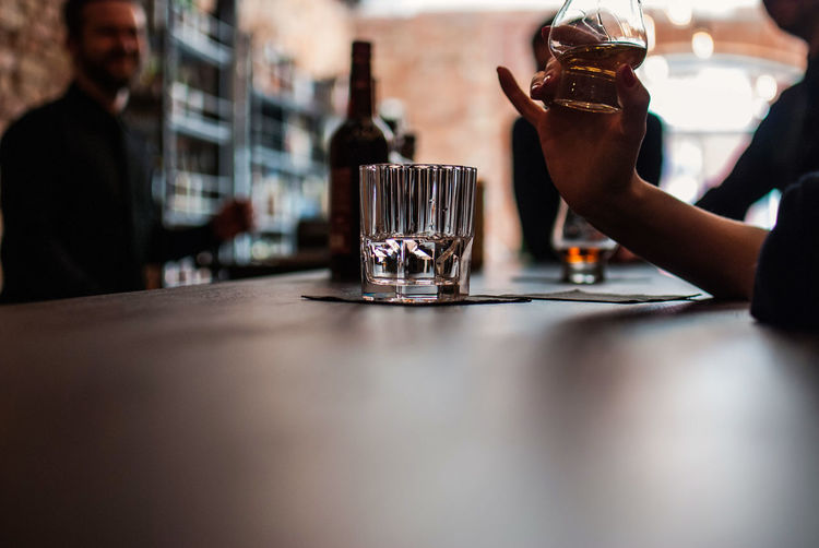 Cropped image of woman drinking whiskey at table in bar