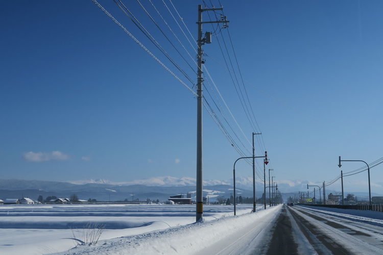 Electricity pylon by road against sky during winter