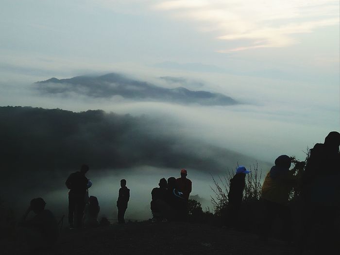 Silhouette people at mountains against cloudy sky