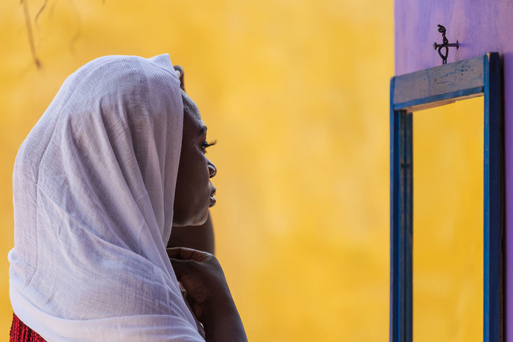 African ghana woman standing in front of a mirror with a white shawl covering her hair