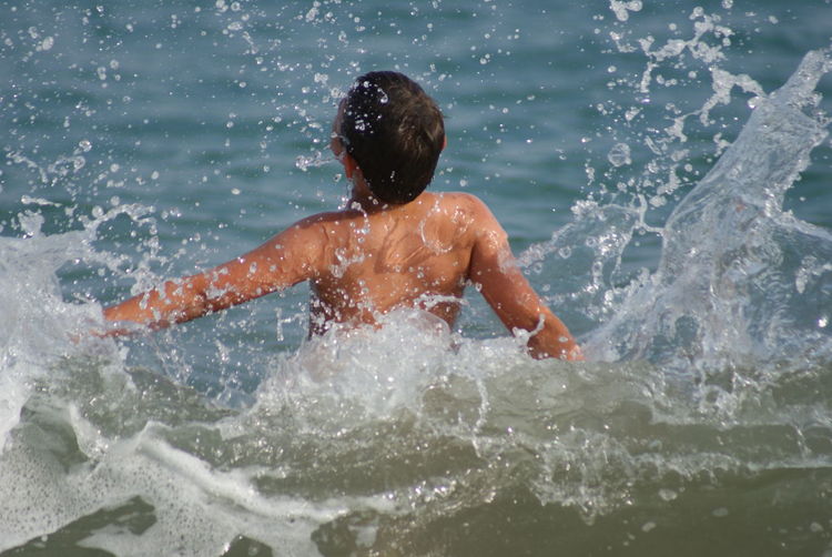 Rear view of shirtless boy enjoying sea wave