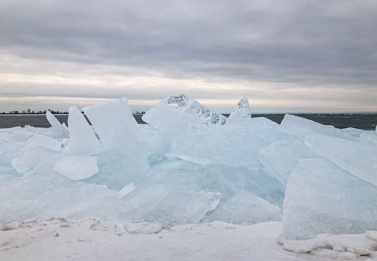 Large flat pieces of ice piled up along the shore of a lake in winter.