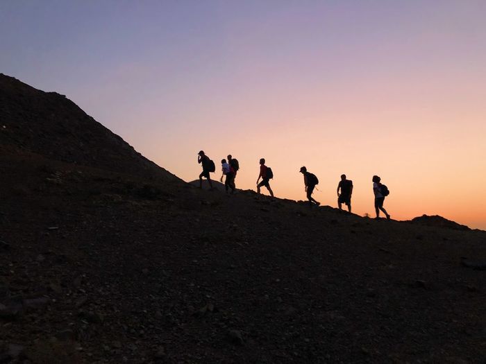 Group of people on mountain against sky during sunset