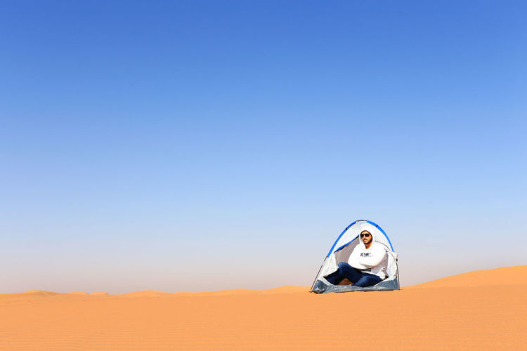 Man sitting in tent on desert against clear sky