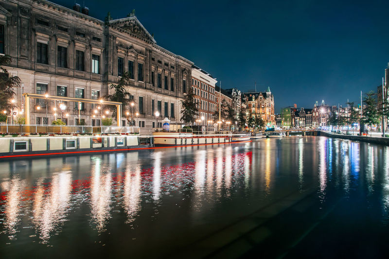 Illuminated buildings by river against sky in city at night