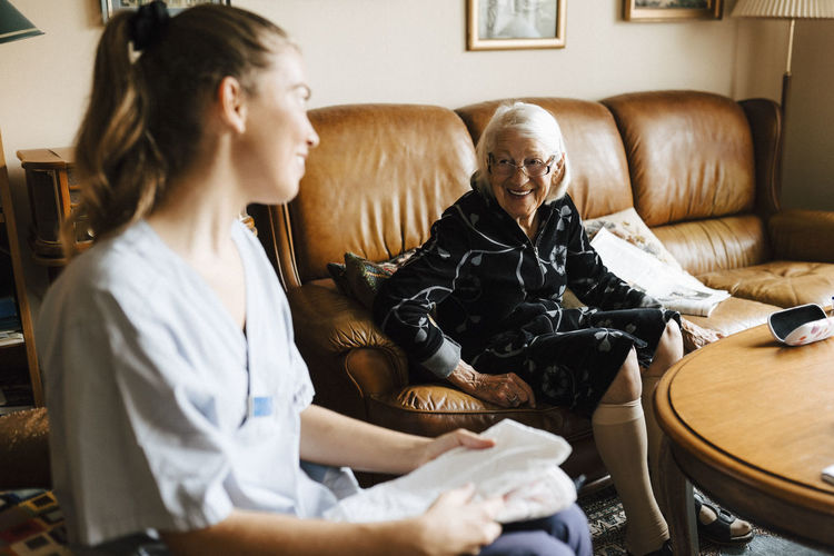 Smiling senior woman talking with female healthcare while sitting in living room at home