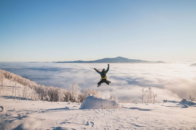 Energetic boy in winter clothes jumping from a stump into the fresh snow with a view of the sunrise