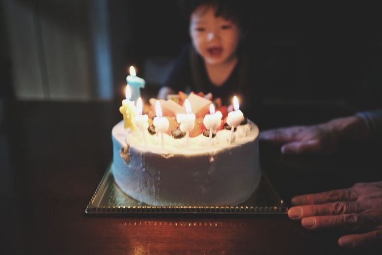 Cropped hand by cake with baby boy in background
