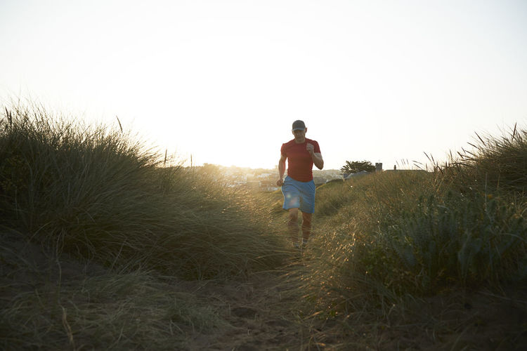 Mature athlete running amidst grass on sand dune