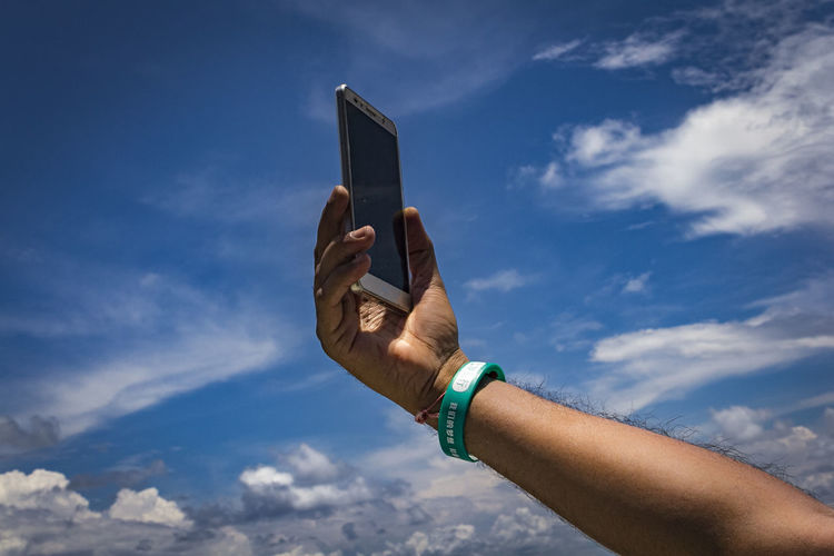 Cropped hand of man holding mobile phone against sky