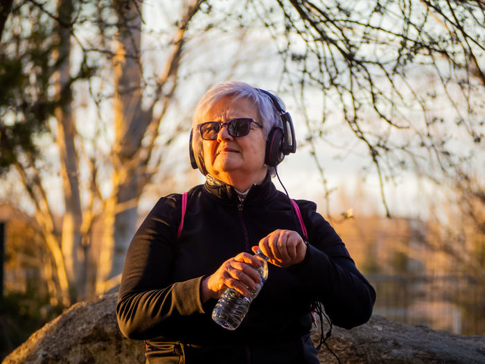 Senior woman listening music in park during sunset