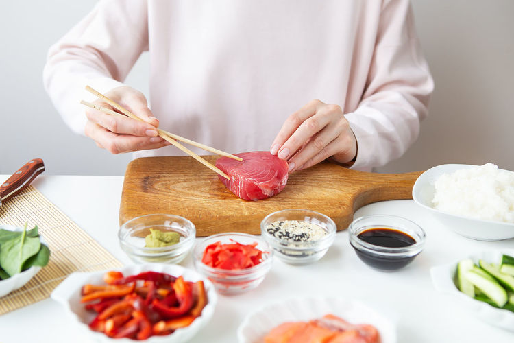 Sushi preparation process, girl holding tuna with chopsticks.