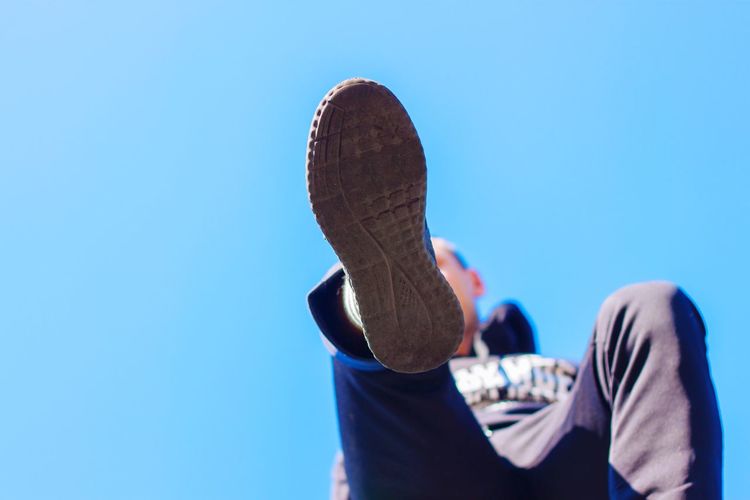 Low angle view of man wearing shoe against clear blue sky