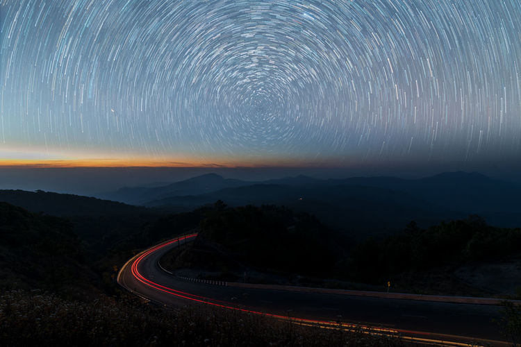 Light trails on road against starry sky at night