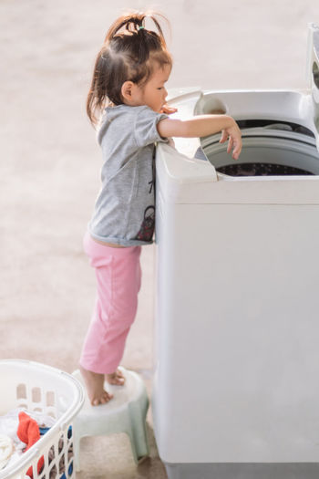 Full length of girl standing by washing machine
