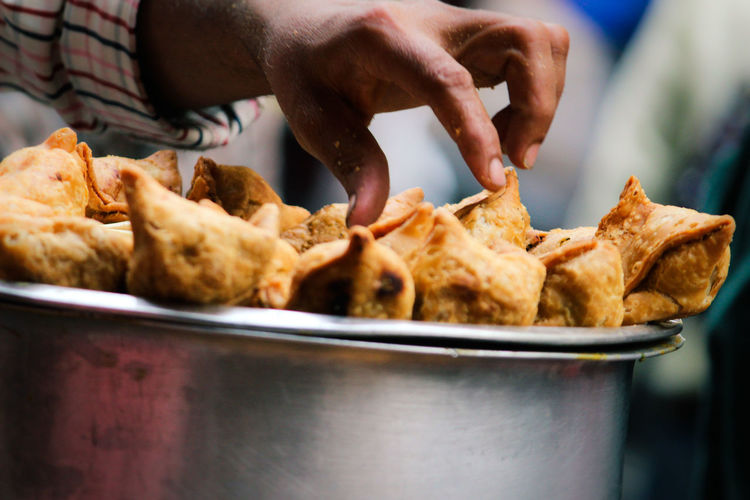 Cropped hand touching samosas in container