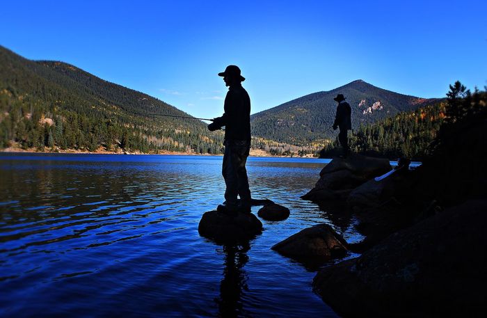 Silhouette man fishing in river against blue sky