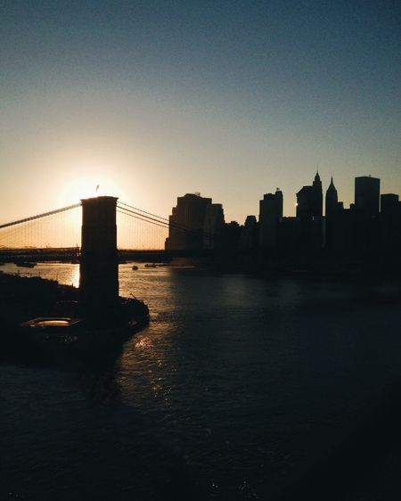 Silhouette of suspension bridge in city at sunset