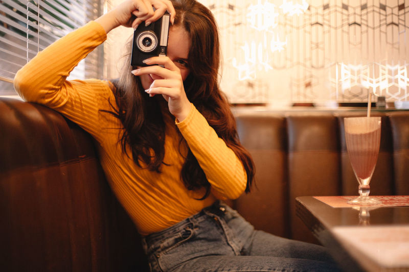 Happy teenage girl photographing with vintage camera in cafe