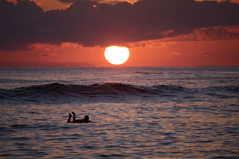 Silhouette man swimming in sea against sky during sunset