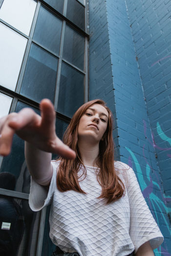Low angle portrait of young woman standing against wall