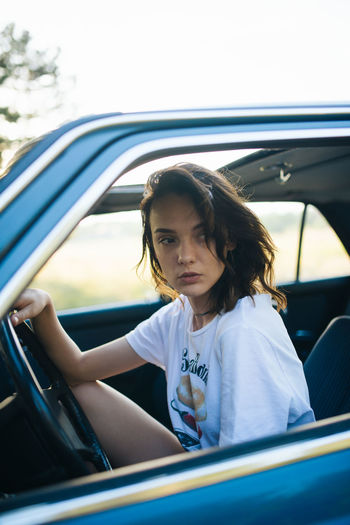 Young woman sitting in a parked vintage car.