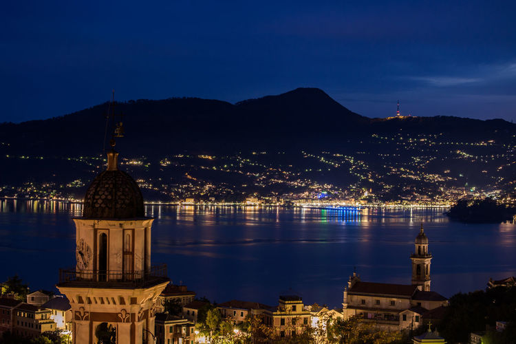 Illuminated town by sea at rapallo against sky