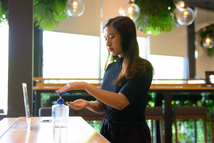 Side view of young woman standing by table at cafe