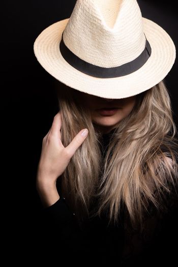 Close-up of woman wearing hat against black background