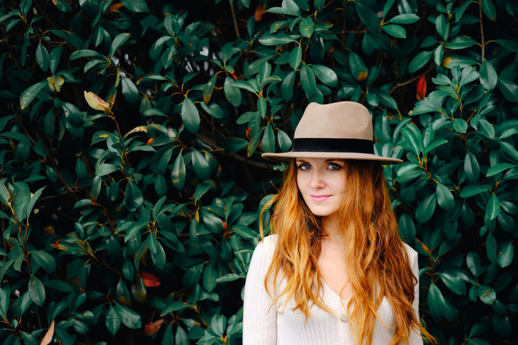 Portrait of woman wearing hat standing against plants