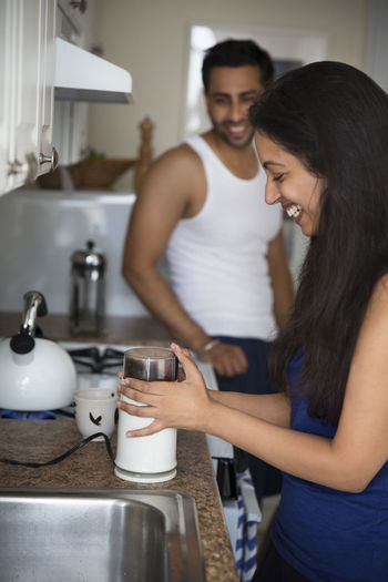 Man looking at woman making coffee while standing in kitchen