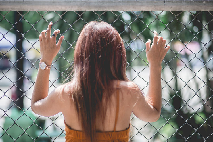 Rear view of woman standing against chainlink fence