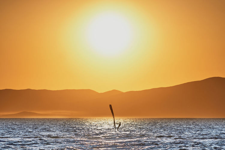 Scenic view of sea with windsurfer against orange sky